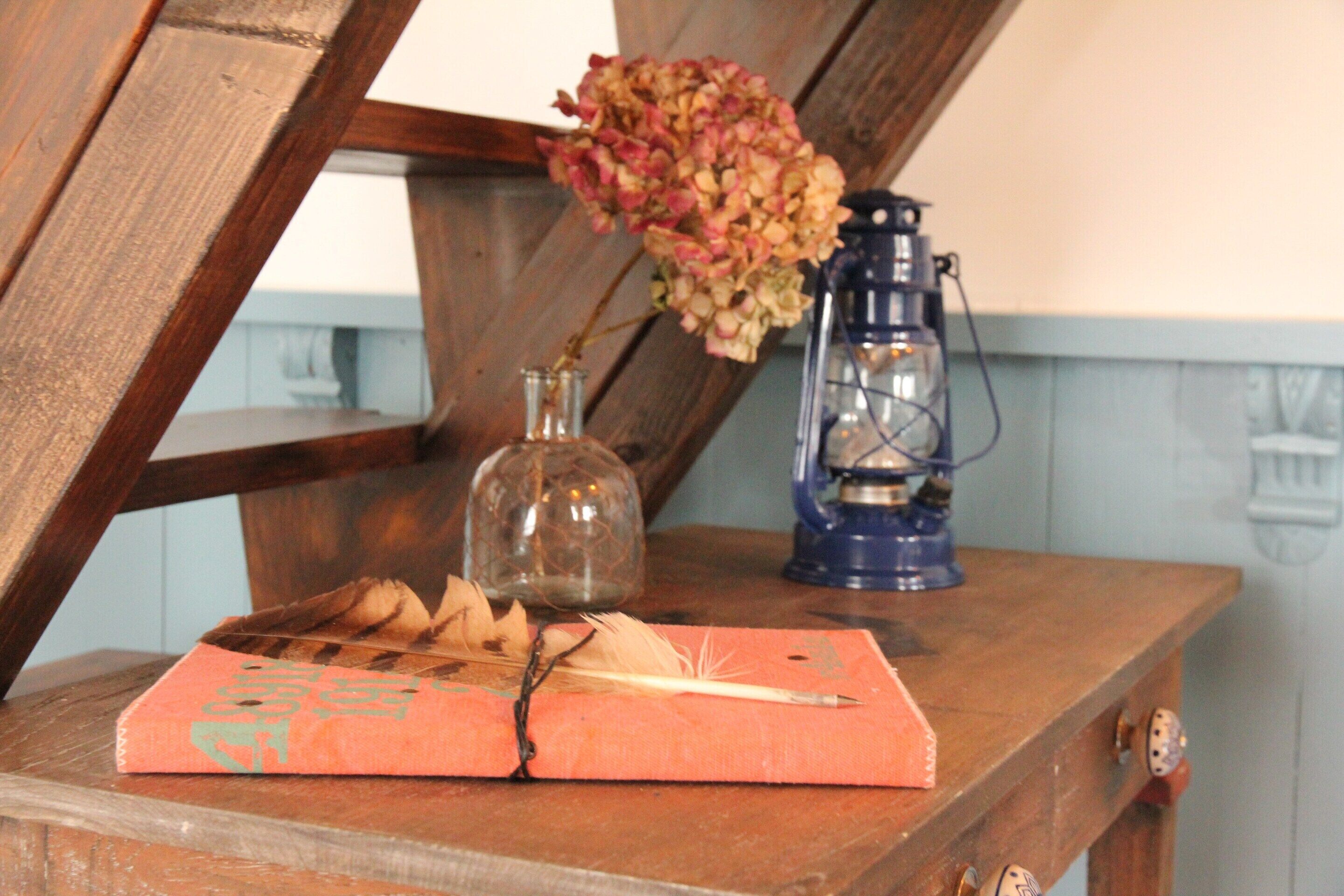 A wooden table with a book, feather quill, and lantern.