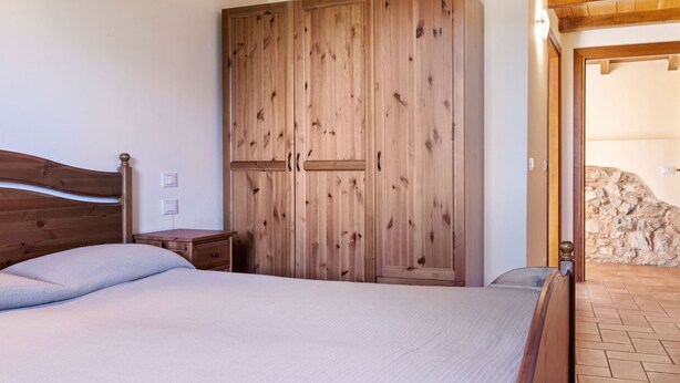 A bedroom with a wooden wardrobe, a bed with a headboard, and a stone wall. - Spacious Holiday Home in Ca' De' Grimaldi near Town Center (Castellarano)