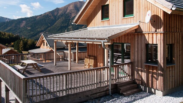 Una baita in legno con una veranda, un patio coperto e uno sfondo montuoso.