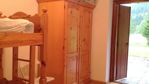 Quarto com cama de madeira, um guarda-roupa e porta que dá para uma varanda.