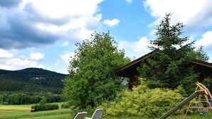 A rustic cabin with a swing set and two lounge chairs in a grassy field. - Vintage Holiday Home in Grafenried With Garden (Drachselsried)