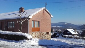 A brick house with a sloped roof and a chimney, surrounded by snow-covered ground and a clear blue sky. - Holiday Home in Stavelot Near Tennis Court (Stavelot)