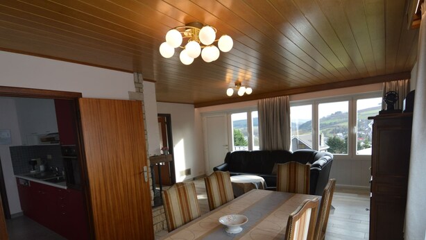 A dining area with a long table, chairs, and a chandelier. There is a kitchen visible through an open door. - Holiday Home in Stavelot Near Tennis Court (Stavelot)