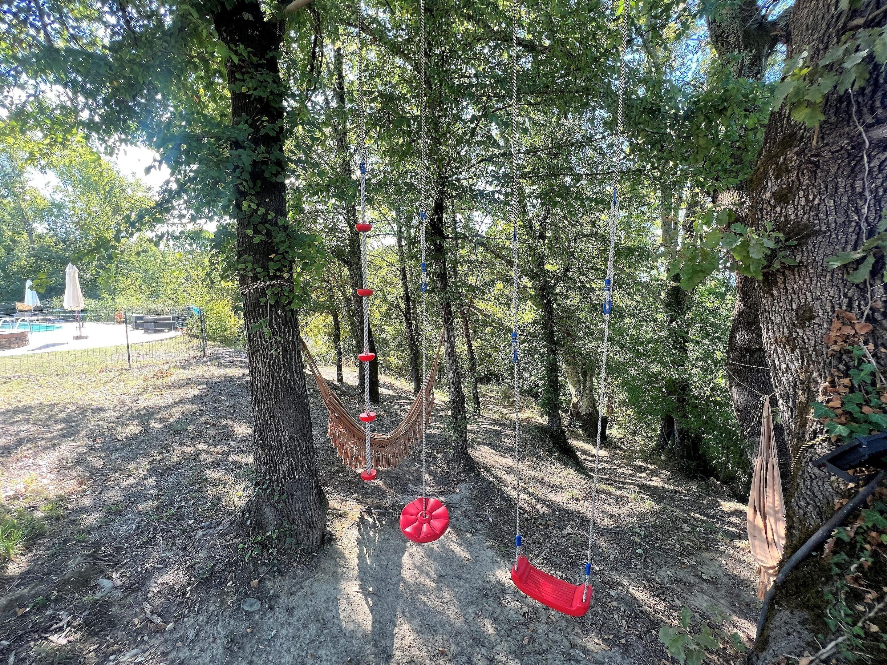 A forested area with a hammock swing and a swing set.