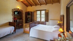 A bedroom with a bed, a crib, a wooden chair, a table with a lamp, a fireplace, and a window. - Farmhouse in Aulla With Private Pool (Aulla)