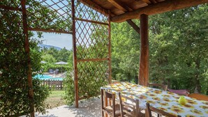 A covered patio with a table and chairs, surrounded by greenery and a pool in the background. - Farmhouse in Aulla With Private Pool (Aulla)