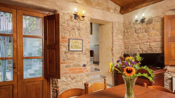 A rustic stone wall interior with a wooden dining table, a vase with flowers, and a television on a wooden cabinet. - Farmhouse in Aulla With Private Pool (Aulla)