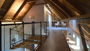 A high-ceilinged wooden interior with a glass railing staircase, a seating area with chairs, and a visible fire extinguisher.