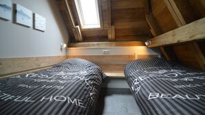 A small, cozy room with two beds, wooden beams, a skylight, and a wall-mounted light fixture.