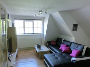 A modern loft-style living room with a black leather sofa, a small wooden coffee table, and a large window providing natural light. - Alpine Stay in Wildemann (Clausthal-Zellerfeld)