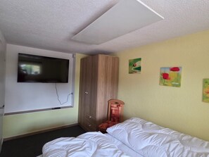 Quarto de hotel com cama, guarda-roupa, televisão na parede e uma pequena mesa.