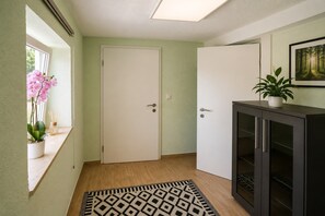 A hallway with a white door, a dark cabinet, a patterned rug, and a potted plant. - Ski- und Wanderurlaub im Wald Ferienhaus Adlerblick (Masserberg)