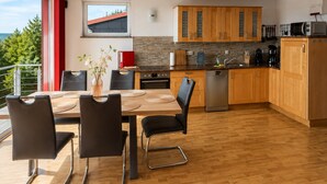 A modern kitchen with wooden cabinets, a dining table with chairs, and a view of the outdoors. - Ski- und Wanderurlaub im Wald Ferienhaus Adlerblick (Masserberg)