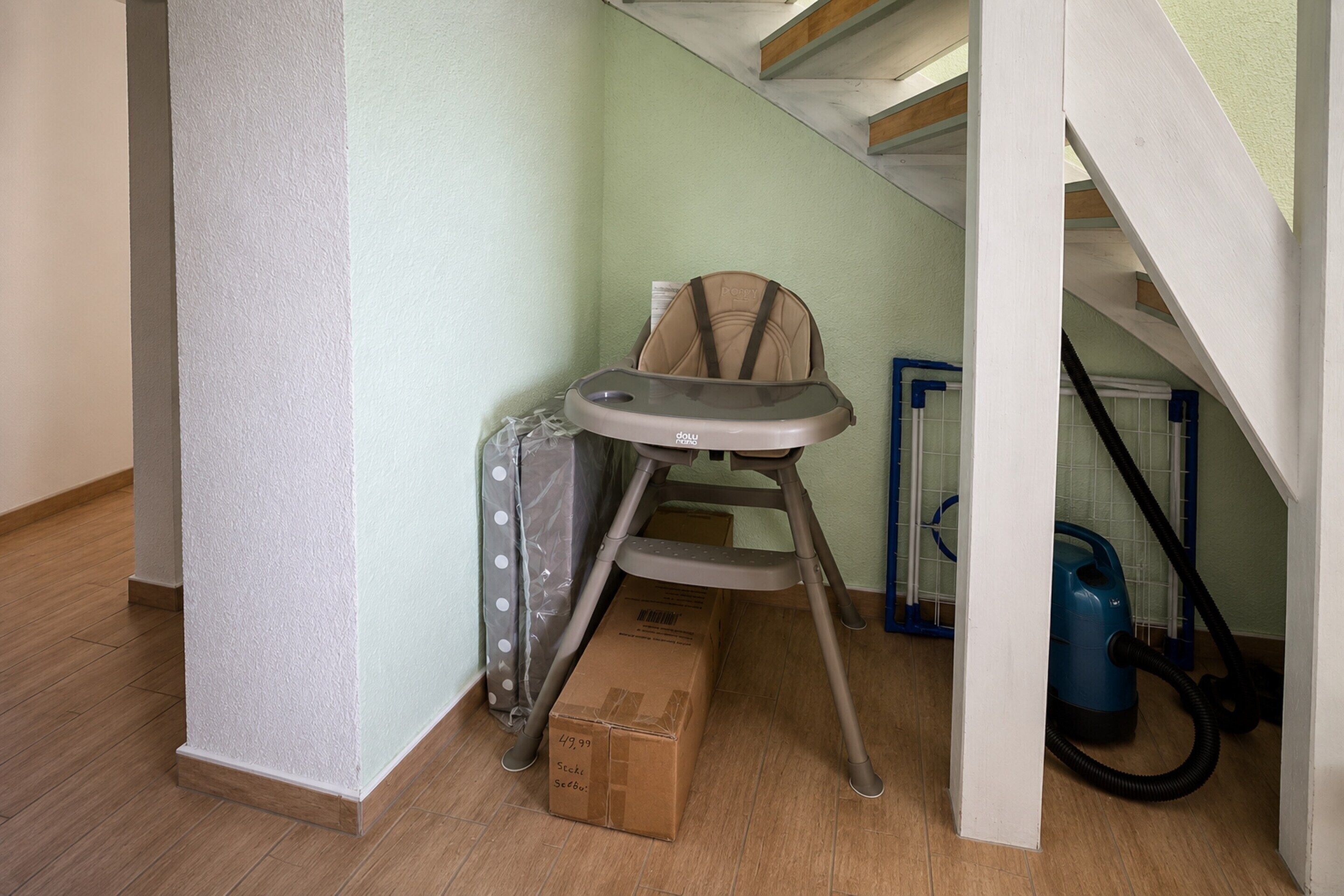 Un rincón de una habitación con una trona para bebé, un aspirador y una caja de cartón.