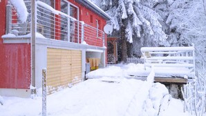 Un bâtiment rouge avec une porte jaune, entouré d’arbres couverts de neige et d’une clôture blanche.