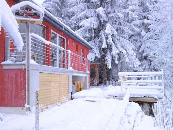 A red building with a yellow door, surrounded by snow-covered trees and a white fence. - Ski- und Wanderurlaub im Wald Ferienhaus Adlerblick (Masserberg)