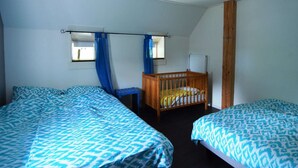 A bedroom with two beds, a wooden crib, a window with blue curtains, and a white radiator. - Beautiful Farmhouse in Wapse With Fenced Garden (Wapse)
