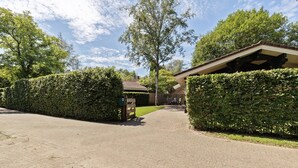 Une allée pavée mène à une maison dotée d’un porche et d’une haie bien entretenue.