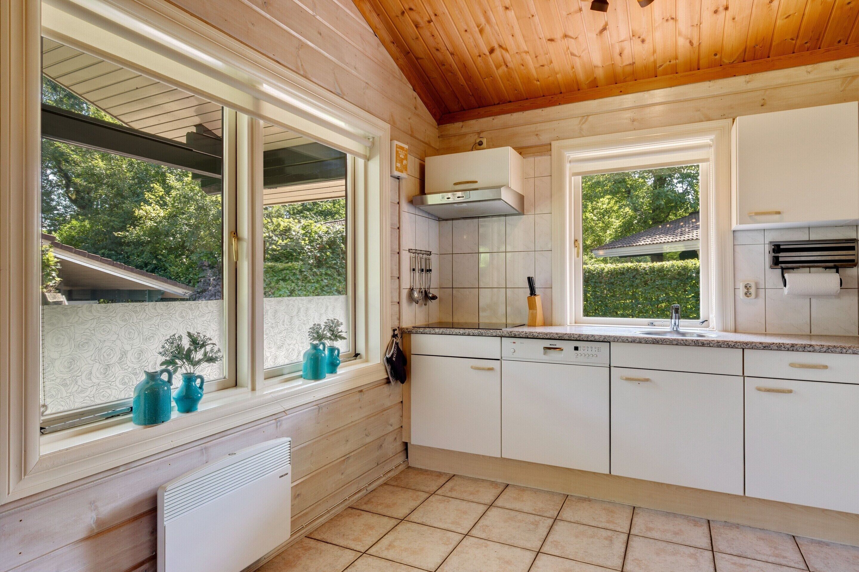 A kitchen with white cabinets, a window with a view of greenery, and a wooden ceiling.