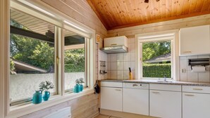 Une cuisine avec des meubles blancs, une fenêtre donnant sur un paysage verdoyant et un plafond en bois.
