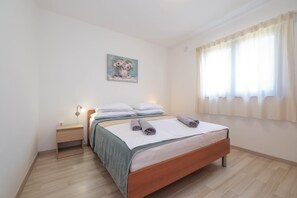 A bedroom with a wooden bed, a nightstand, a lamp, a painting on the wall, and a window with curtains. - Peace & Sun Await in Dalmatia (Starigrad)