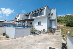 A modern two-story house with a balcony, outdoor seating, and potted plants.