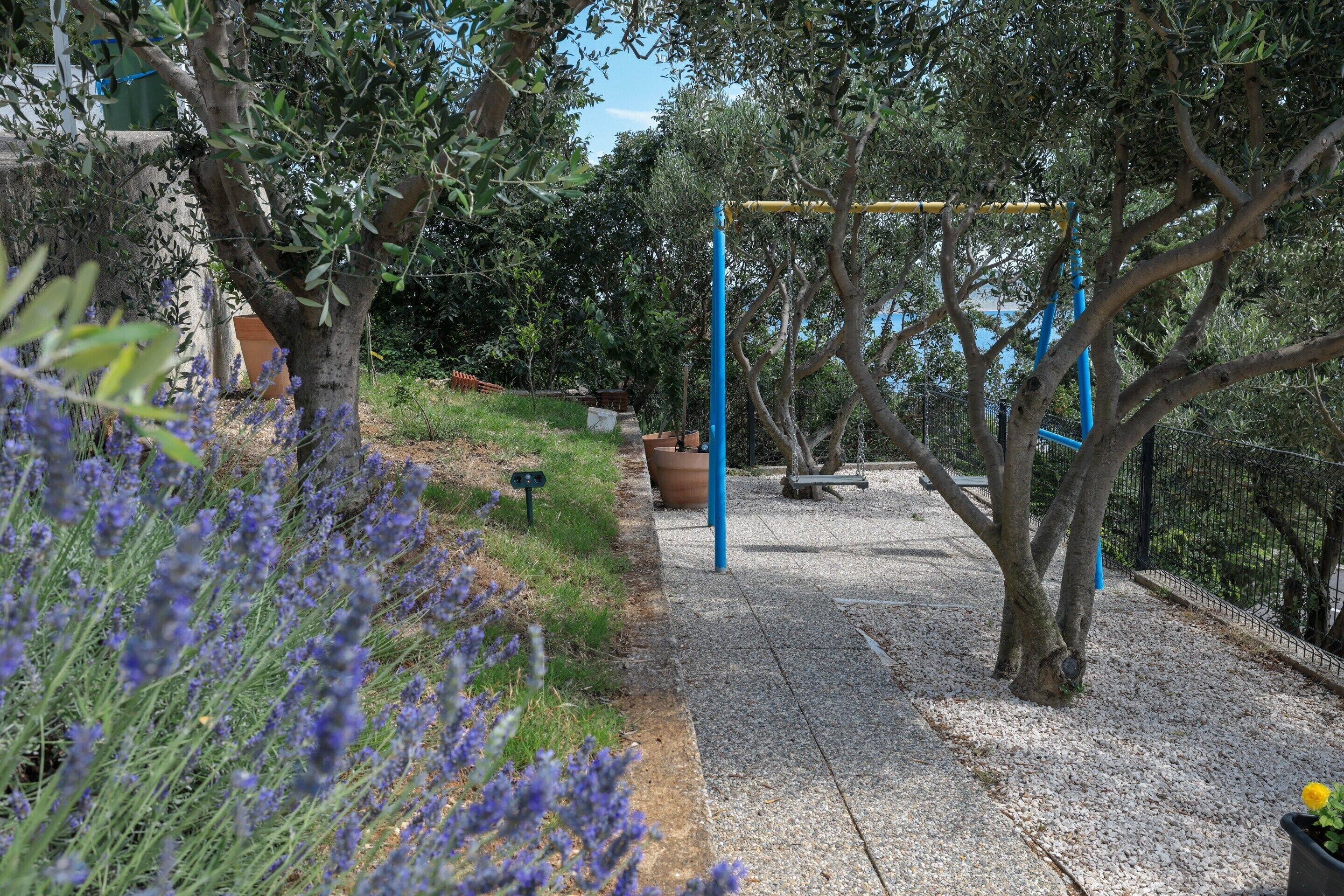 A garden with a swing set, a gravel path, and lavender bushes.