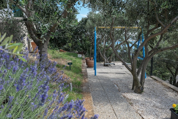 A garden with a swing set, a gravel path, and lavender bushes.