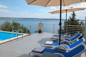 A poolside area with lounge chairs, a pool, and a view of the sea.