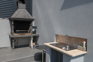 An outdoor kitchen with a built-in grill, a sink, and a tiled backsplash.