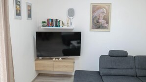 A living room with a flat-screen TV, a grey sofa, a bookshelf with books and decorative items, and a framed painting on the wall. - Peace & Sun Await in Dalmatia (Starigrad)