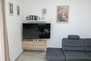 A living room with a flat-screen TV, a grey sofa, a bookshelf with books and decorative items, and a framed painting on the wall. - Peace & Sun Await in Dalmatia (Starigrad)