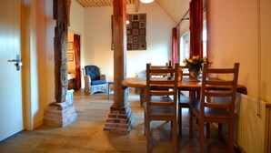 A dining area with a wooden table and chairs, a hanging light fixture, and a brick column. - Romantic Farmhouse Escape (Geesteren)