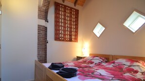 A bedroom with a wooden bed, a quilt, a brick wall, and a window. - Romantic Farmhouse Escape (Geesteren)