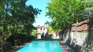 A swimming pool with a stone wall on one side and a wooden fence on the other, surrounded by greenery. - Peaceful Retreat With Shared Pool (San Marcello Piteglio)