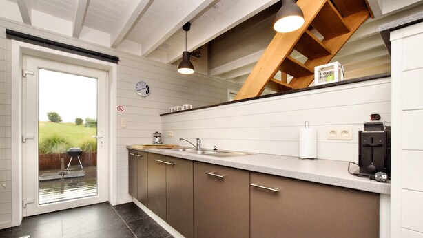 A modern kitchen with a large island, a built-in oven, and a view of the outdoors through a glass door. - Holiday Home Suitable for Families With Sauna (Houffalize)