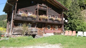 A traditional wooden chalet with a balcony, a stone foundation, and outdoor seating. - Chalet in Matrei Near Ski Lift & Bus (Matrei in Osttirol)