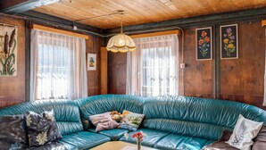 A cozy room with a teal leather sofa, a wooden ceiling, and floral artwork on the walls. - Chalet in Matrei Near Ski Lift & Bus (Matrei in Osttirol)