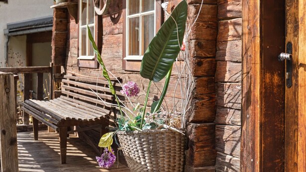 A wooden bench and a large woven planter with flowers on a wooden deck. - Chalet in Matrei Near Ski Lift & Bus (Matrei in Osttirol)