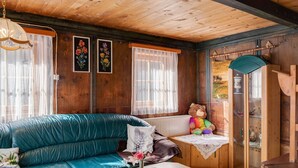 A cozy room with a wooden ceiling, a teal leather sofa, a wooden cabinet with glass doors, and a teddy bear. - Chalet in Matrei Near Ski Lift & Bus (Matrei in Osttirol)