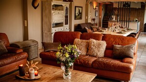 En hyggelig stue med en brun lædersofa, et træbord med stearinlys og en vase med blomster.