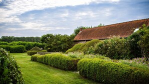 En velholdt have med pænt beskåret hæk og et traditionelt hus med rødt tegltag.