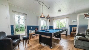 Um quarto com mesa de bilhar, poltronas de couro e um sofá.