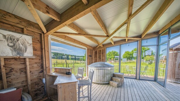 Een houten terras met een hottub, een houten tafel en een stoel.