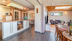 Een moderne keuken met een centraal eiland, een eetgedeelte met houten stoelen, en een woonkamer met een bank en een televisie.