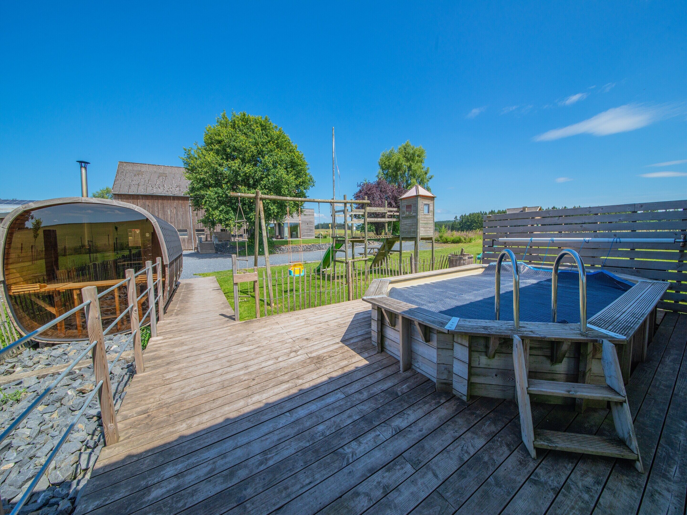 Une terrasse en bois avec un jacuzzi, une balançoire et un espace de jeux.