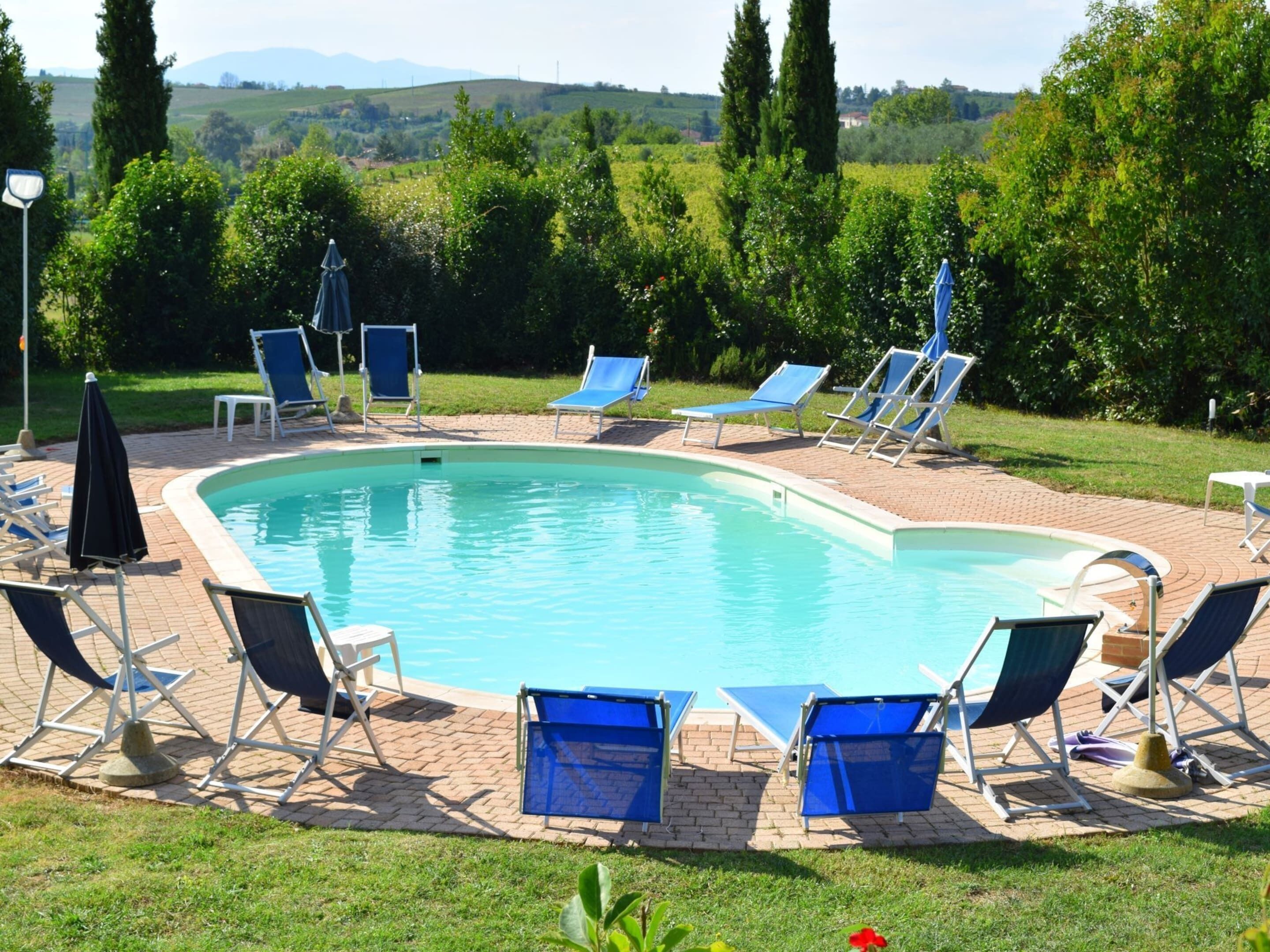 A rectangular swimming pool with blue lounge chairs and umbrellas arranged around it.