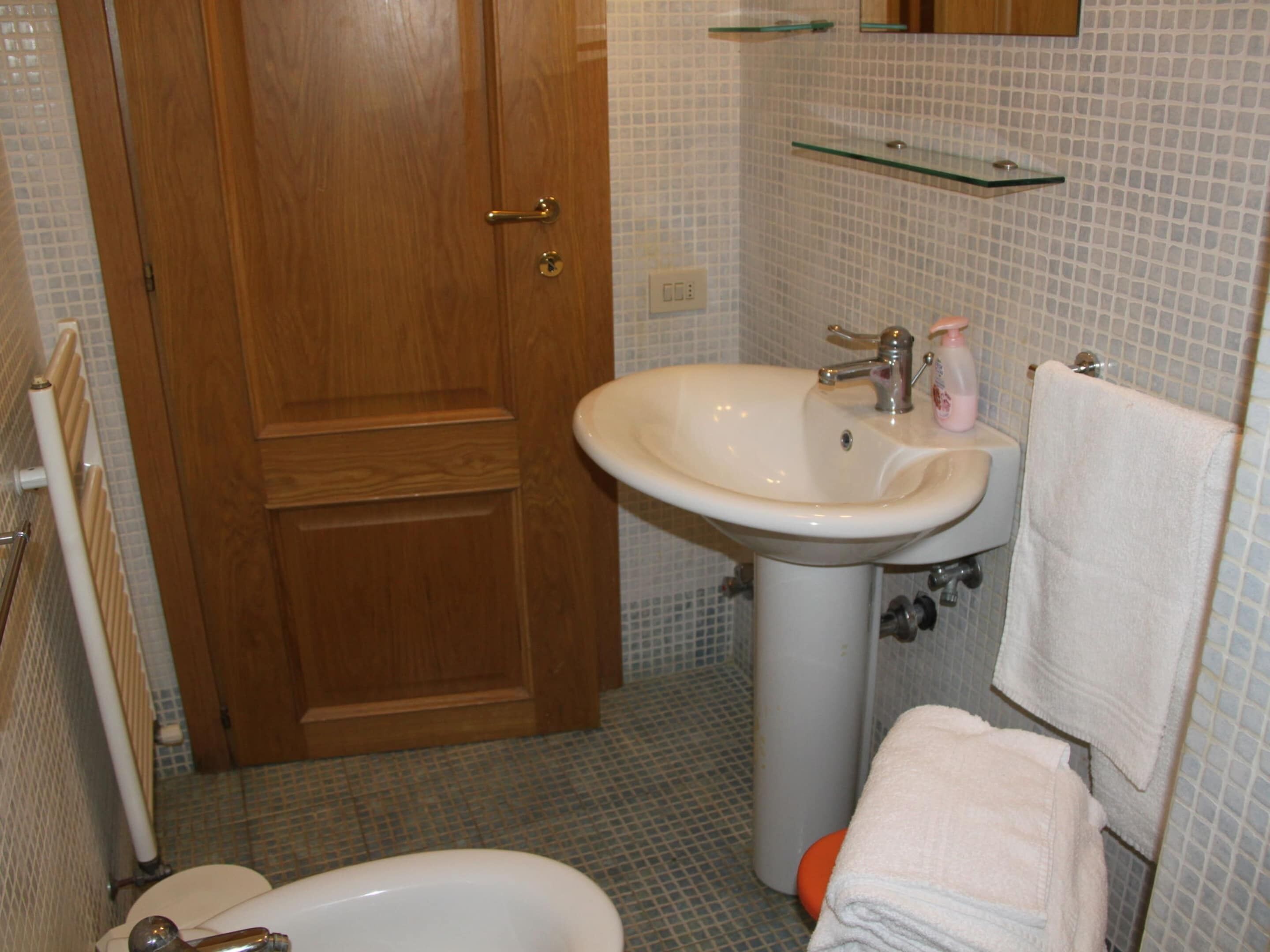 Un baño con puerta de madera, un lavabo blanco con espejo, un perchero y un inodoro.