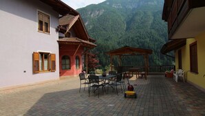 A courtyard with a wooden pergola, outdoor seating, and a mountain backdrop. - Holiday Home in Caldes Near Ski Lift (Caldes)