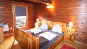 En stuga med träpanel, ett rum med en säng, två sängbord, ett fönster och en värmare.